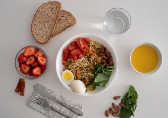 A balanced meal featuring a variety of healthy ingredients including noodles, eggs, almonds, strawberries, and fresh vegetables.