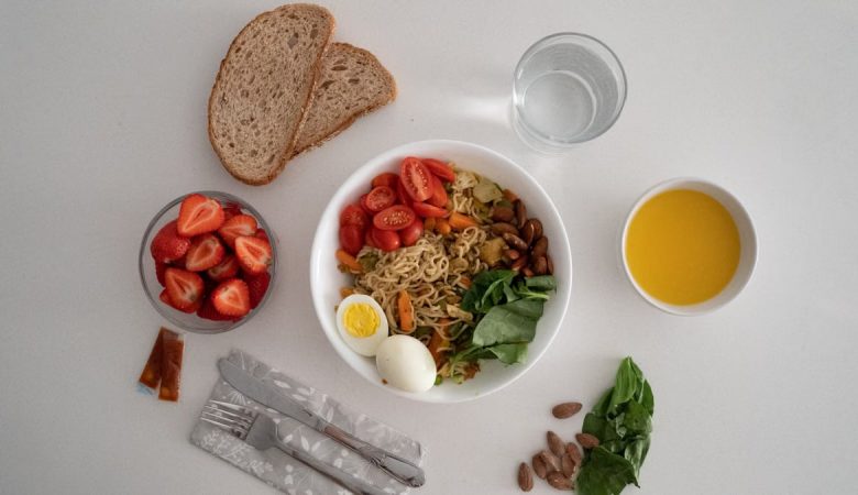 A balanced meal featuring a variety of healthy ingredients including noodles, eggs, almonds, strawberries, and fresh vegetables.